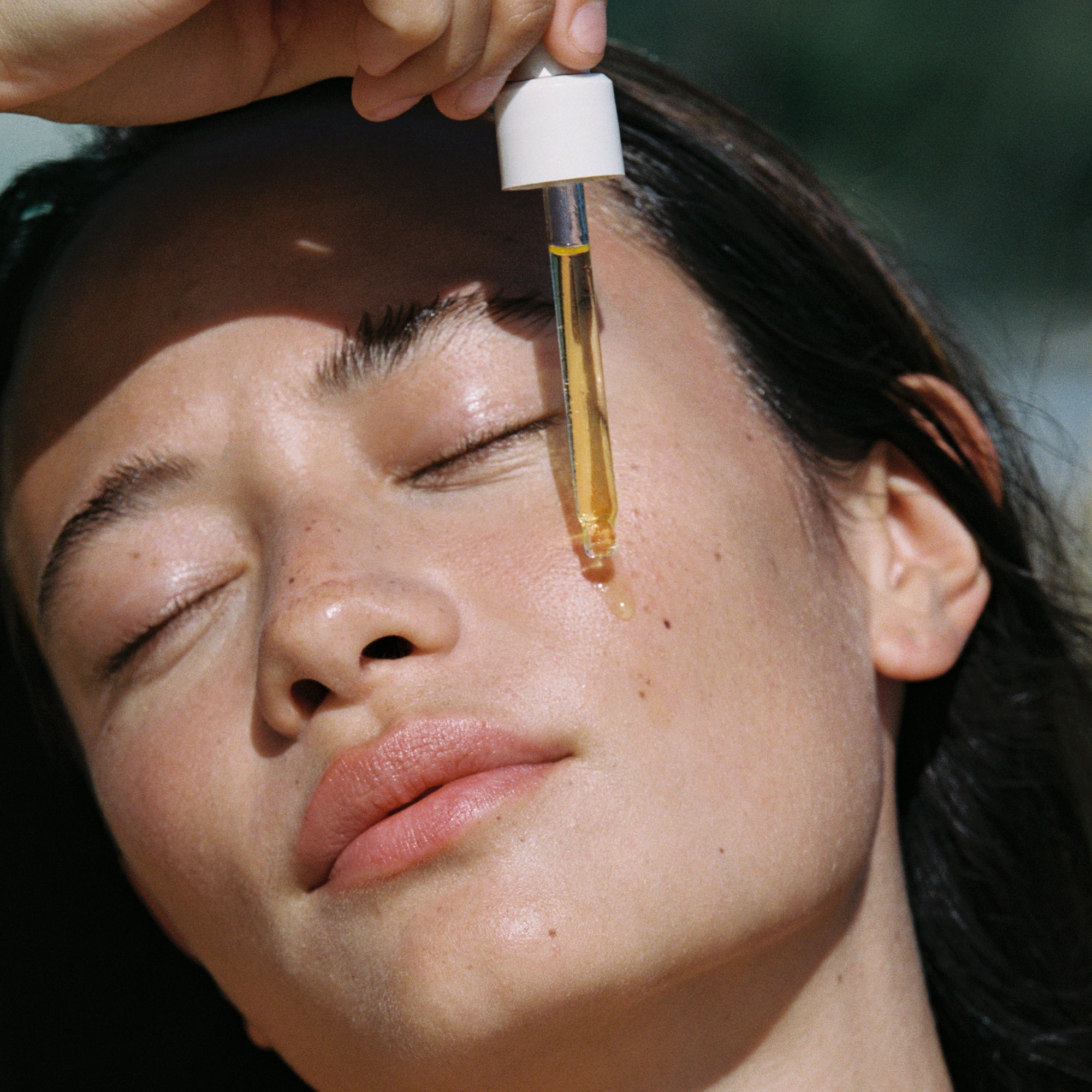 Person applying a dropper of liquid to their face