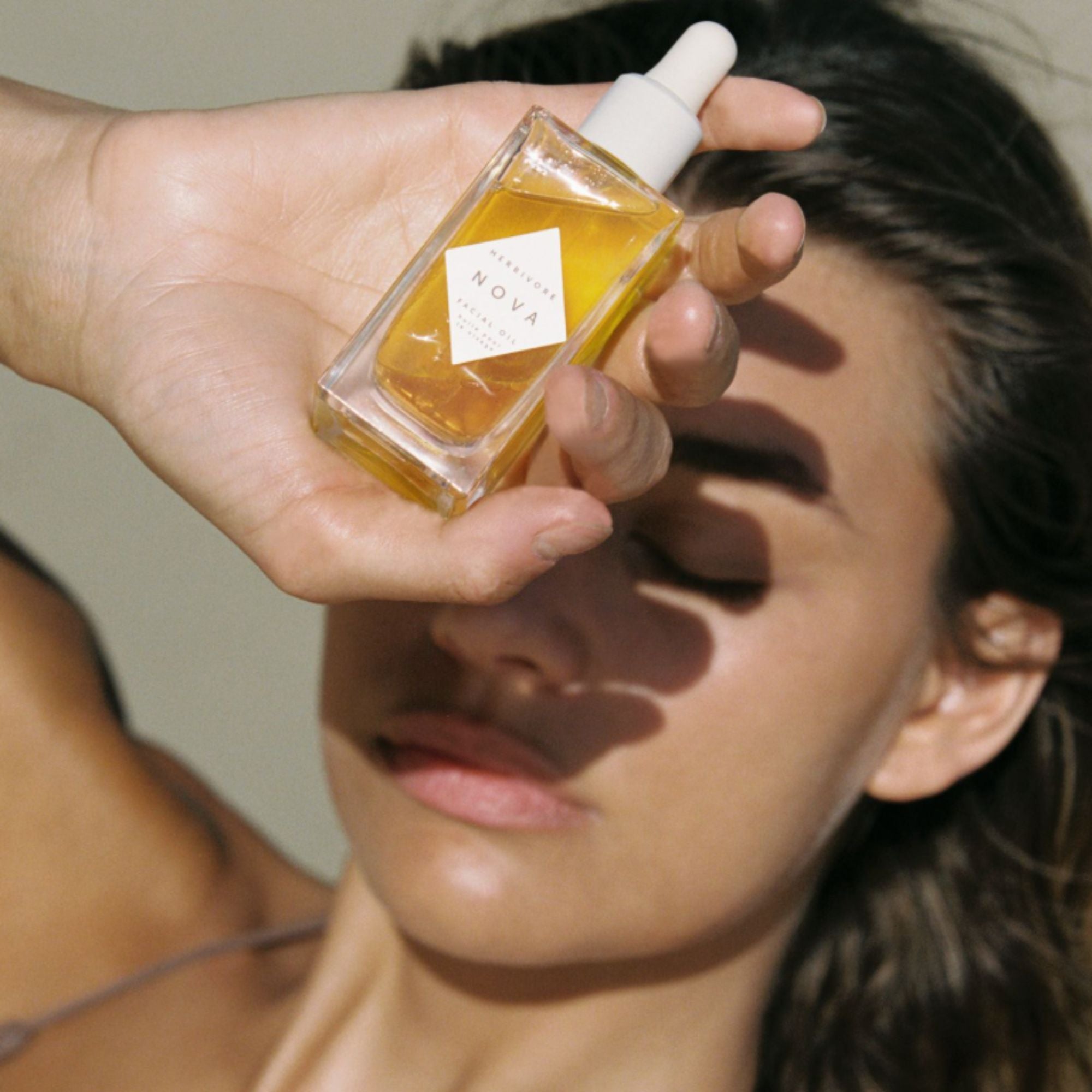 Person holding a small bottle of oil close to their face with a neutral background