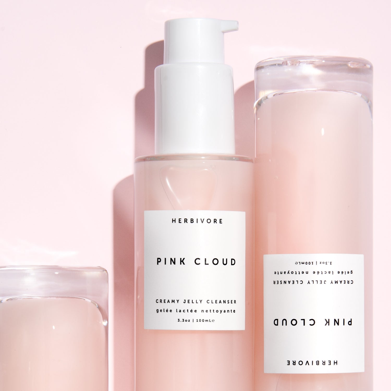 Close-up of three Pink Cloud Creamy Jelly Cleanser Bottles against pink background