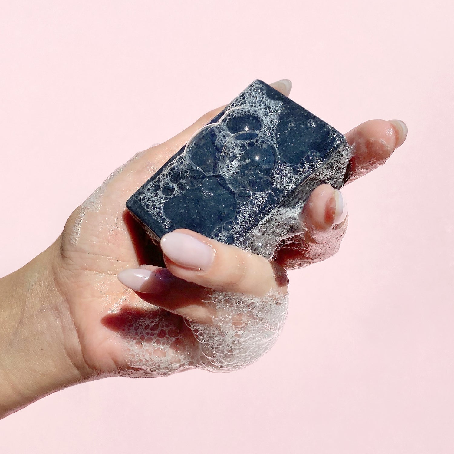 A hand holding a foaming bar of Bamboo Charcoal Detox Soap